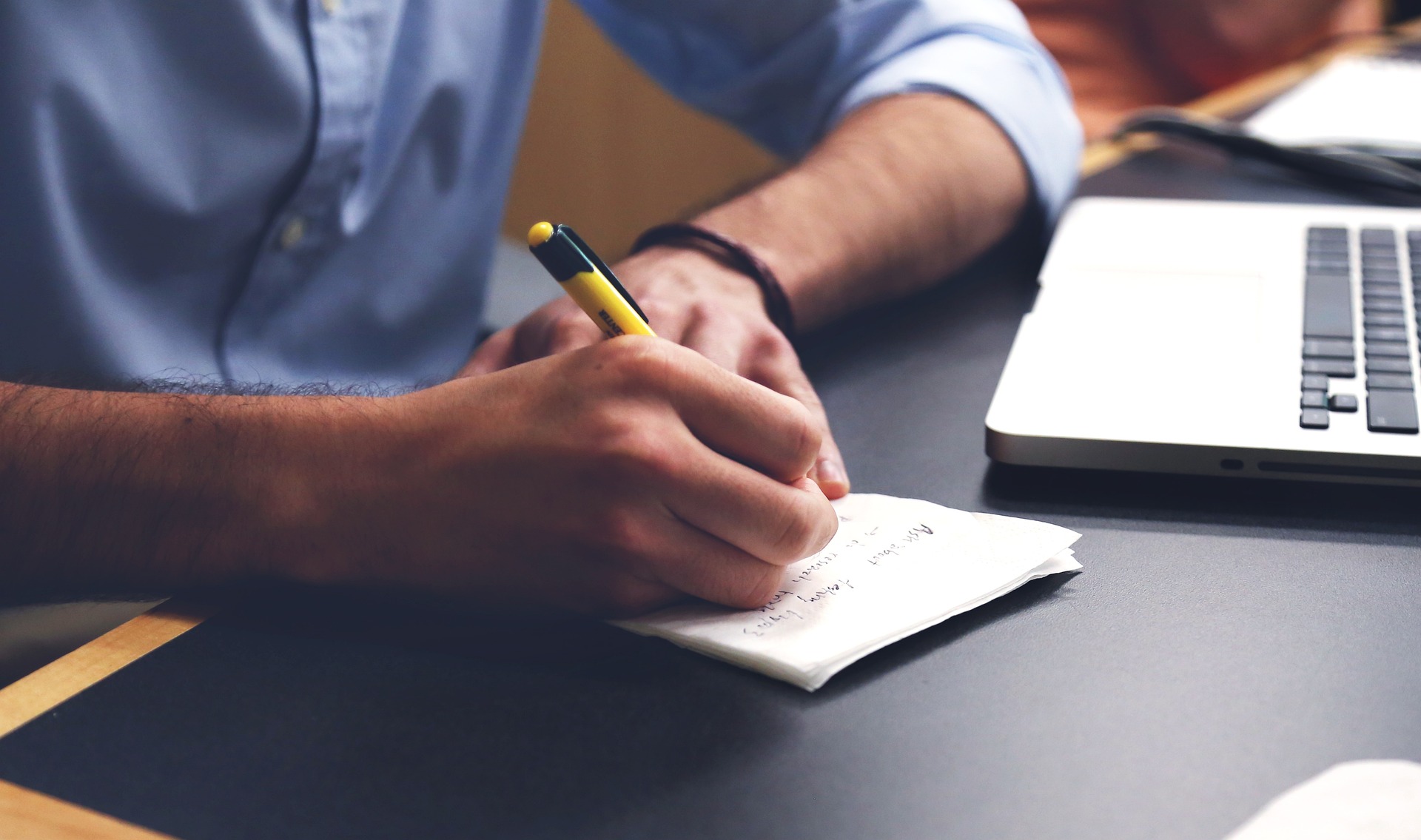 Office worker taking notes on a cocktail napkin while sitting at a table with others